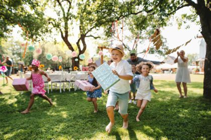 Small children ruunning with present outdoors in garden on birthday party.